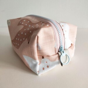 May include: A small pink and white zippered pouch with a light blue zipper pull. The pouch has a repeating pattern of stylized deer with white spots.