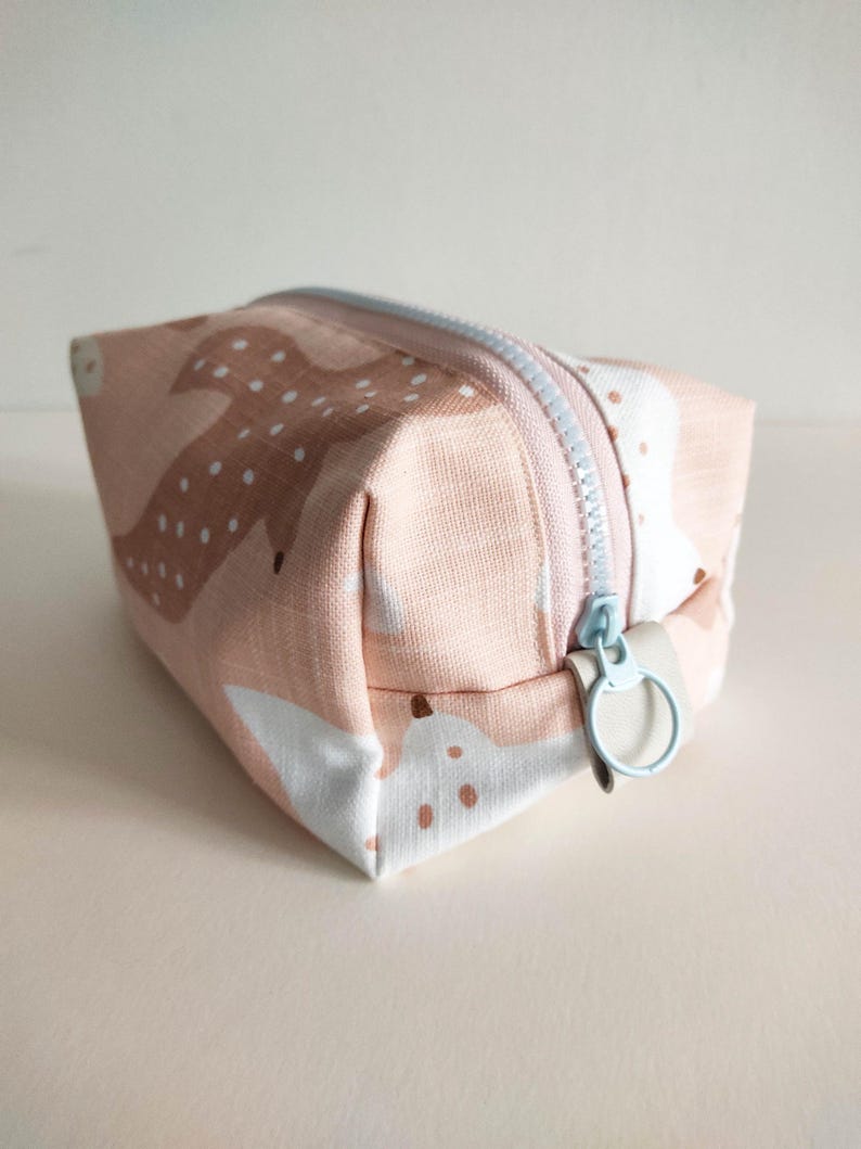 May include: A small pink and white zippered pouch with a light blue zipper pull. The pouch has a repeating pattern of stylized deer with white spots.