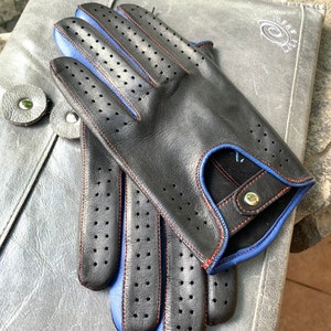 May include: Black leather driving gloves with blue and red stitching. The gloves have a perforated design and a button closure.