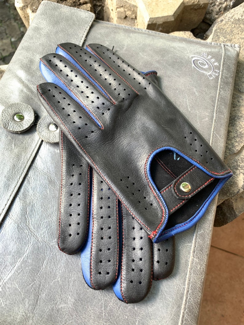 May include: Black leather driving gloves with blue and red stitching. The gloves have a perforated design and a button closure.
