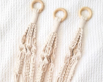 May include: Three macrame plant hangers with wooden rings. The hangers are made of natural cotton cord and have a simple, minimalist design.