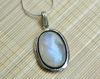 May include: A silver chain necklace with a silver oval pendant featuring a large, iridescent moonstone.