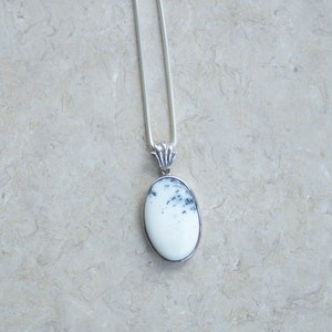 May include: A silver pendant necklace featuring an oval-shaped, white stone with black speckles. The stone is set in a silver bezel and hangs from a delicate silver chain. The pendant has a decorative silver bail.