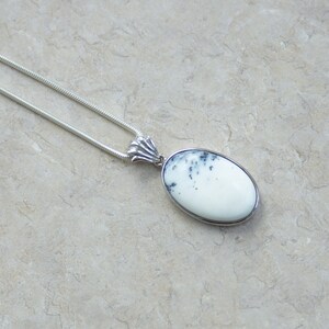 May include: A silver necklace featuring an oval pendant with a white stone and black speckles. The pendant is set in a silver bezel and hangs from a delicate silver chain. The jewelry is displayed on a neutral background.