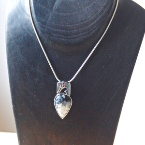 Puede incluir: Un collar de cadena de plata con un colgante en forma de l&aacute;grima con una piedra de &aacute;gata negra y blanca engastada en plata. El colgante tiene un peque&ntilde;o acento de piedra roja.