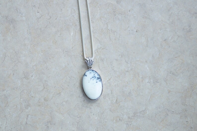 May include: A silver pendant necklace featuring an oval-shaped, white stone with black speckles. The stone is set in a silver bezel and hangs from a delicate silver chain. The pendant has a decorative silver bail.