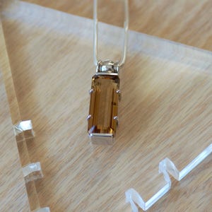 May include: A silver chain necklace with a pendant featuring a rectangular, brown gemstone.