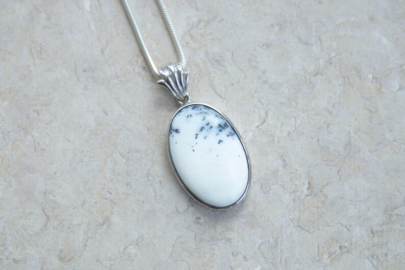 May include: A silver pendant necklace featuring an oval-shaped white stone with black speckles. The stone is set in a silver bezel and hangs from a silver chain. The pendant has a decorative silver bail.