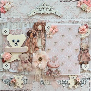 May include: A scrapbook page featuring a cream-colored teddy bear cutout with the word STORY, a plush teddy bear, two illustrated dolls in coats, a pink butterfly-patterned card, a pincushion, lace trim, white buttons, and peach-colored fabric flowers.