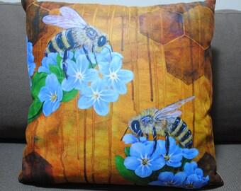May include: Square decorative pillow featuring two bees and blue flowers against a honeycomb and dripping honey background. The bees have black and yellow stripes. The flowers are light blue with green leaves. The background is a mix of brown and yellow.