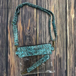 May include: Clear plastic crossbody bag with a teal and black patterned strap. The bag has a zipper closure and a smaller clear pouch with a teal and black patterned strap attached to it.