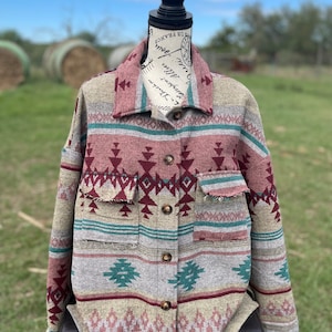 May include: A long-sleeved button-up shirt with a geometric pattern in shades of gray, pink, teal, and brown. The shirt has a relaxed fit and a collar.