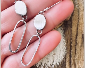 May include: A pair of silver earrings with oval-shaped pendants and textured, open-loop dangles.