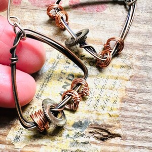May include: A pair of handmade earrings featuring copper wire wrapped around a gear charm. The earrings are made with a combination of copper and silver wire.