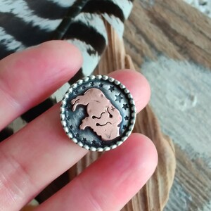 May include: A silver ring with a copper buffalo silhouette design surrounded by a circle of stars.