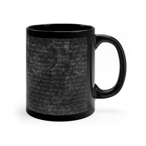 May include: Black ceramic mug featuring a textured, dark gray design with handwritten script. The mug has a curved handle and a glossy finish. The text on the mug is in a light gray color. This mug is perfect for coffee, tea, or any beverage.
