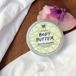 May include: A white tin container with a yellow and green label that reads "KALLIOPE'S BODY BUTTER" in black text. The label also includes the text "ΒΟΥΤΥΡΟ ΣΩΜΑΤΟΣ" in Greek, along with a list of ingredients in Greek. The container is sitting on a wooden surface with a white cloth and pink flower petals.
