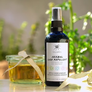 May include: A blue glass bottle with a white label that reads "KALLIOPE'S HERBAL LICE REPELLENT FOR PROTECTION AND TREATMENT APPLE CIDER VINEGAR EUCALYPTUS/ROSE GERANIUM PURE ACTIVE CONSCIOUS". The bottle has a spray nozzle and is sitting on a table with a glass jar and eucalyptus leaves.