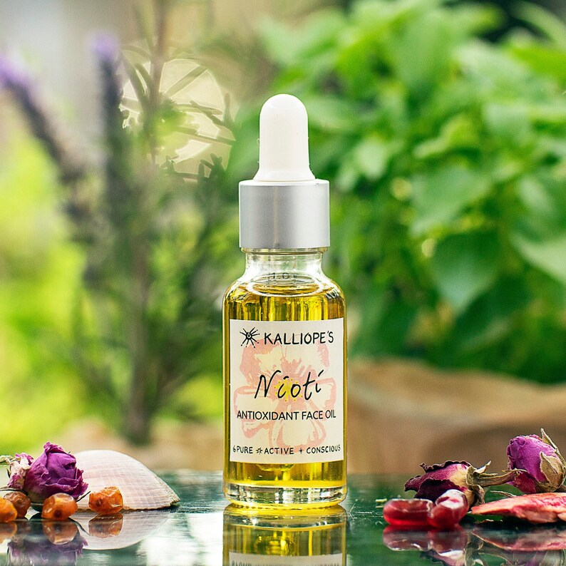 The nioti antioxidant face oil, in a glass 20ml bottle with a dropper. Its colour is bright orange thanks to carotenoids. The backround islush green foliage and it's surounded by pomegranate fruits, seabuckthorn berries and roses.