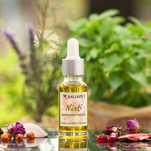 May include: A glass bottle of Nioti Antioxidant Face Oil by Kalliope's. The bottle is clear and has a gold label with the product name and description. The bottle is sitting on a table with a few dried flowers and a seashell.