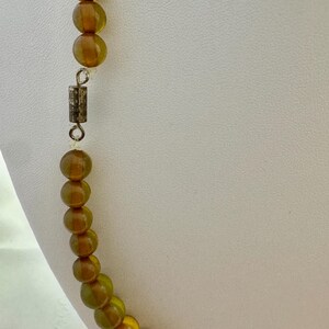 May include: A long necklace made of amber-colored glass beads. The necklace has a silver clasp.