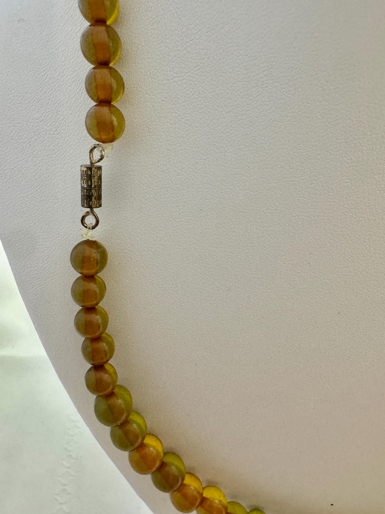 May include: A long necklace made of amber-colored glass beads. The necklace has a silver clasp.