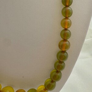May include: A long necklace made of round, green and amber glass beads. The beads are translucent and have a slight shimmer.
