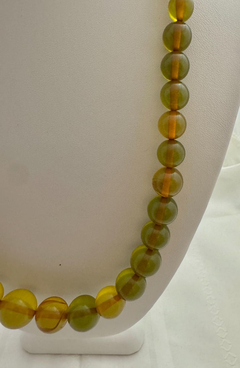 May include: A long necklace made of round, green and amber glass beads. The beads are translucent and have a slight shimmer.