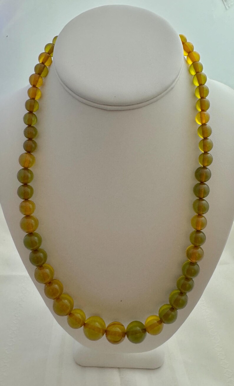 May include: A long necklace made of round, green and amber glass beads.
