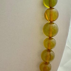 May include: A long necklace made of round, translucent amber beads. The beads are a mix of yellow and green hues, creating a gradient effect.