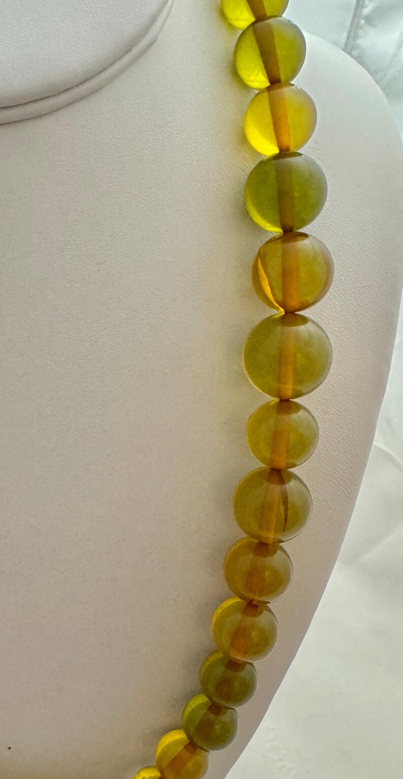 May include: A long necklace made of round, translucent amber beads. The beads are a mix of yellow and green hues, creating a gradient effect.