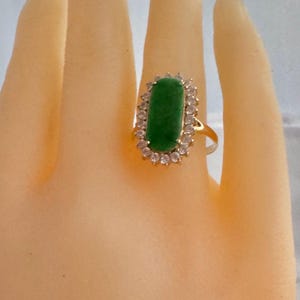 May include: A gold ring with a green gemstone surrounded by a halo of clear stones.