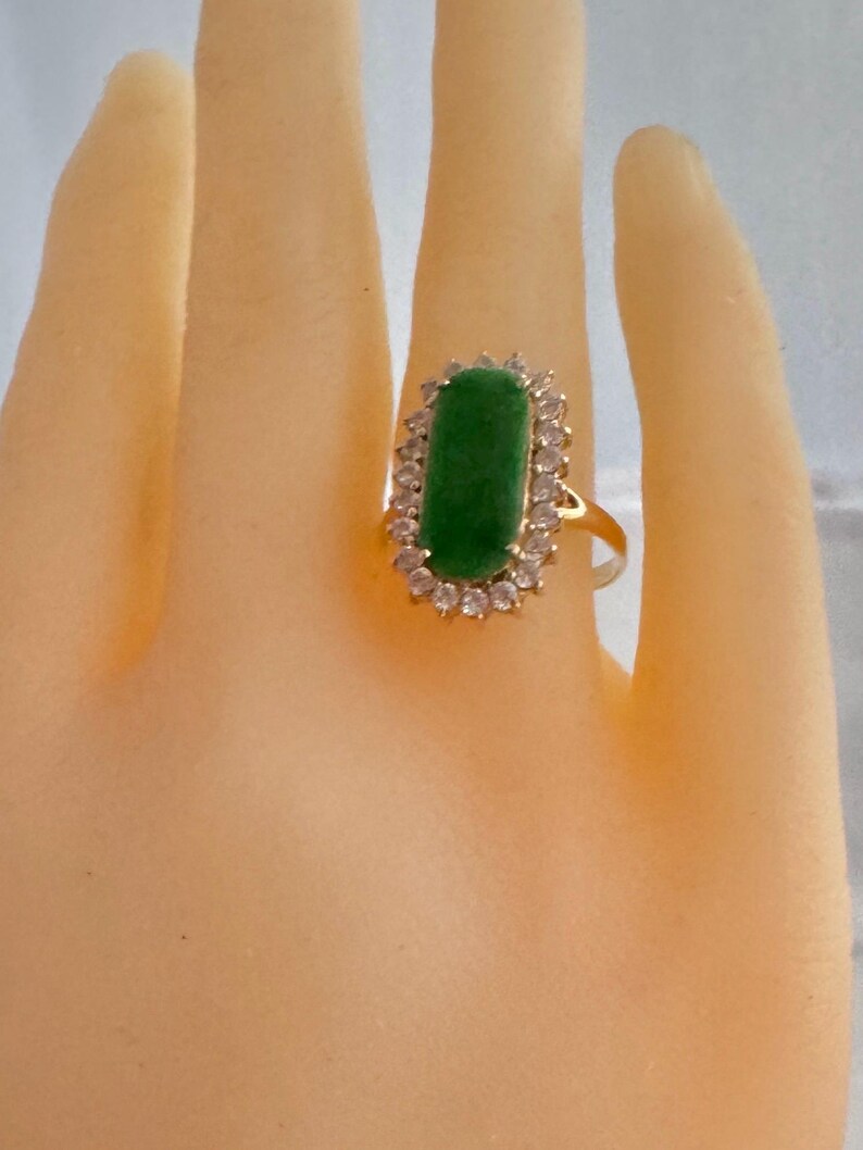 May include: A gold ring with a green gemstone surrounded by a halo of clear stones.