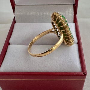 May include: A gold ring with a large green gemstone surrounded by smaller diamonds. The ring is in a red box with white lining.
