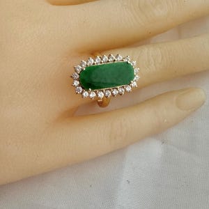 May include: A gold ring with a large, rectangular, green gemstone surrounded by a halo of smaller, clear gemstones.