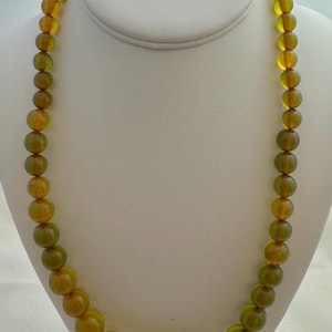 May include: A long necklace made of round, green and amber glass beads.