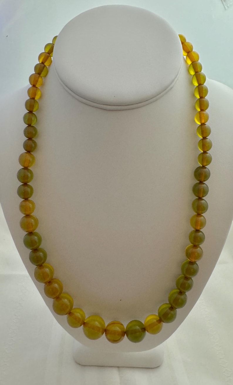 May include: A long necklace made of round, green and amber glass beads.
