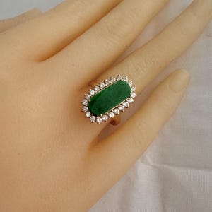 May include: A gold ring with a large, rectangular, green jade stone surrounded by a halo of small, clear diamonds.