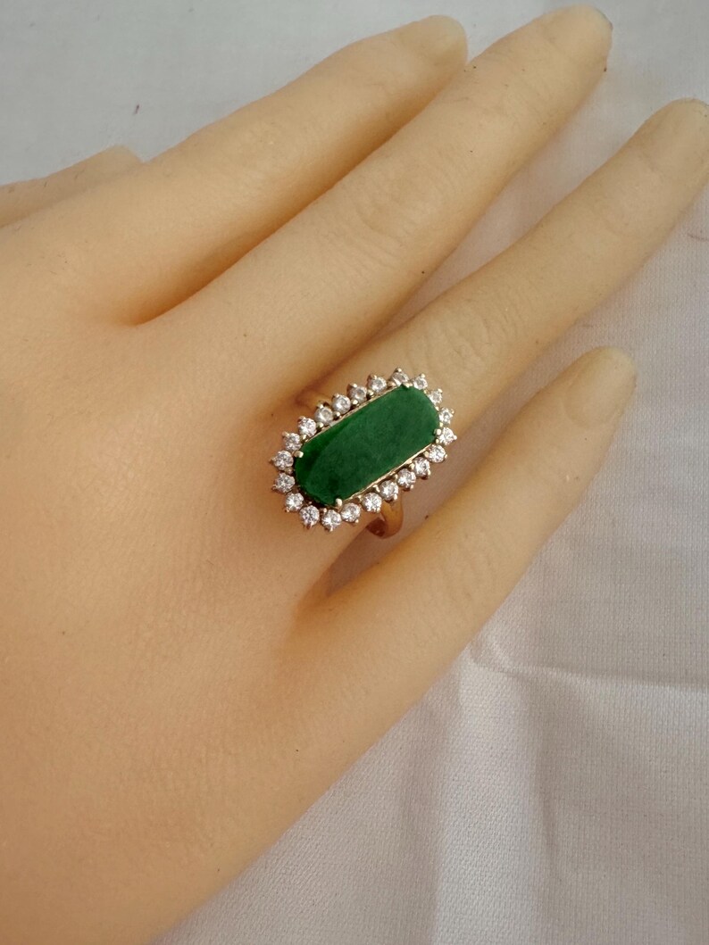 May include: A gold ring with a large, rectangular, green jade stone surrounded by a halo of small, clear diamonds.