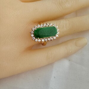 May include: A gold ring with a large, rectangular, green gemstone surrounded by a halo of smaller, clear gemstones.