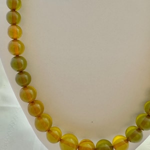 May include: A necklace made of large, round, amber-colored beads with a green hue. The beads are strung on a clear cord.