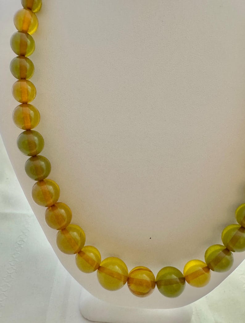 May include: A necklace made of large, round, amber-colored beads with a green hue. The beads are strung on a clear cord.