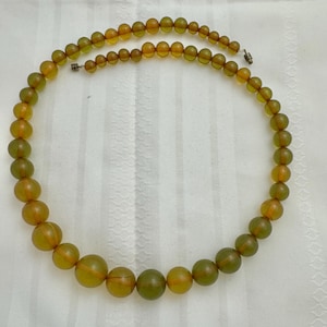 May include: A long necklace made of round, translucent green and amber beads.