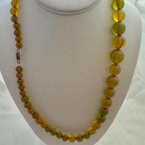 May include: A long necklace made of round, green and amber glass beads. The beads are graduated in size, with the larger beads at the bottom of the necklace.