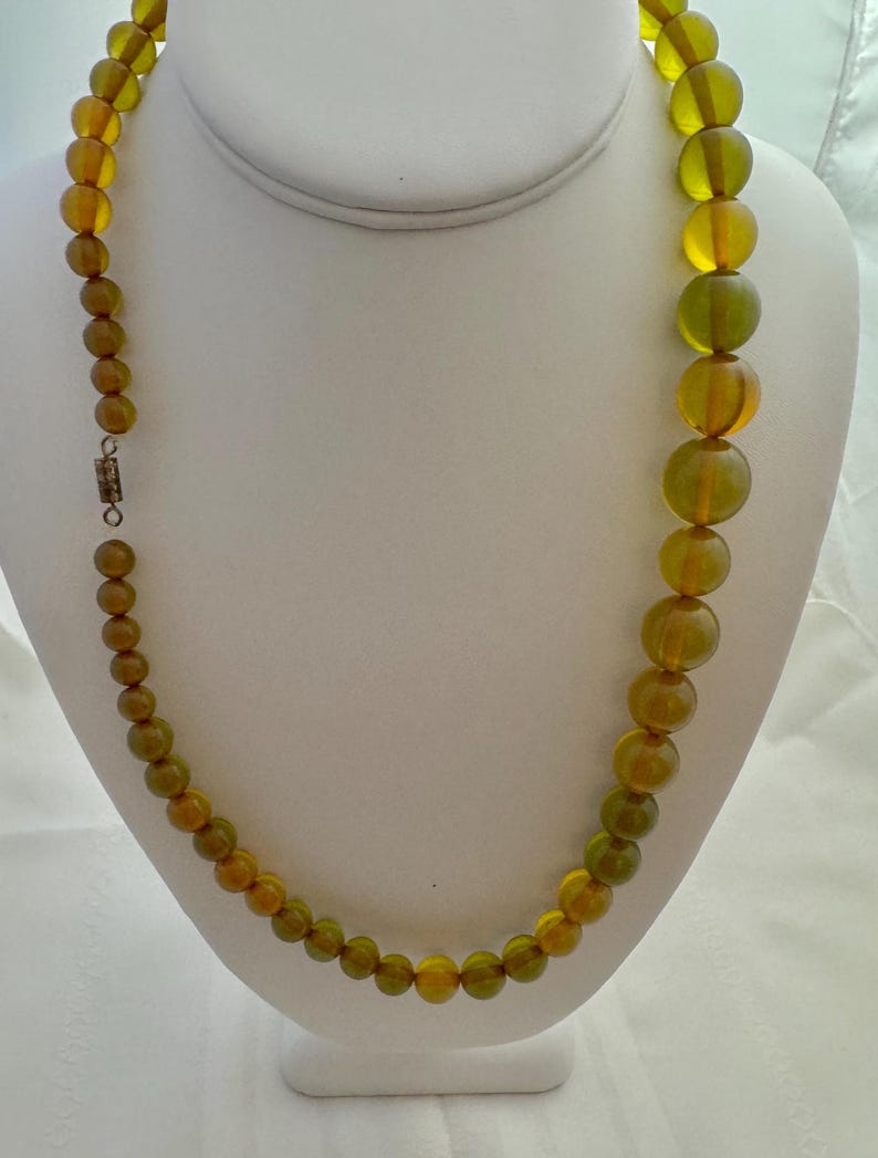 May include: A long necklace made of round, green and amber glass beads. The beads are graduated in size, with the larger beads at the bottom of the necklace.