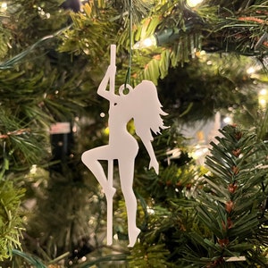 Könnte beinhalten: Weißer Silhouetten-Anhänger einer Person, die auf einer Stange posiert, der an einem Weihnachtsbaum hängt.
