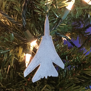 May include: A silver-colored airplane ornament hanging on a Christmas tree with green branches and white lights.