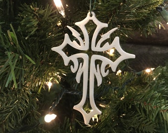 Könnte beinhalten: Weißer, kunstvoll gestalteter Kreuz-Anhänger, der an einem grünen Weihnachtsbaum mit weißen Lichtern hängt.