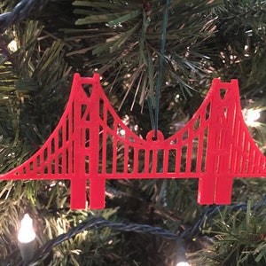 May include: Red plastic ornament shaped like the Golden Gate Bridge, hanging on a Christmas tree.
