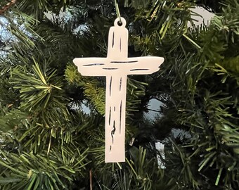Könnte beinhalten: Ein weißer Holz-Kreuz-Anhänger mit rustikalem, abgenutztem Finish. Das Kreuz hängt an einem grünen Weihnachtsbaum.